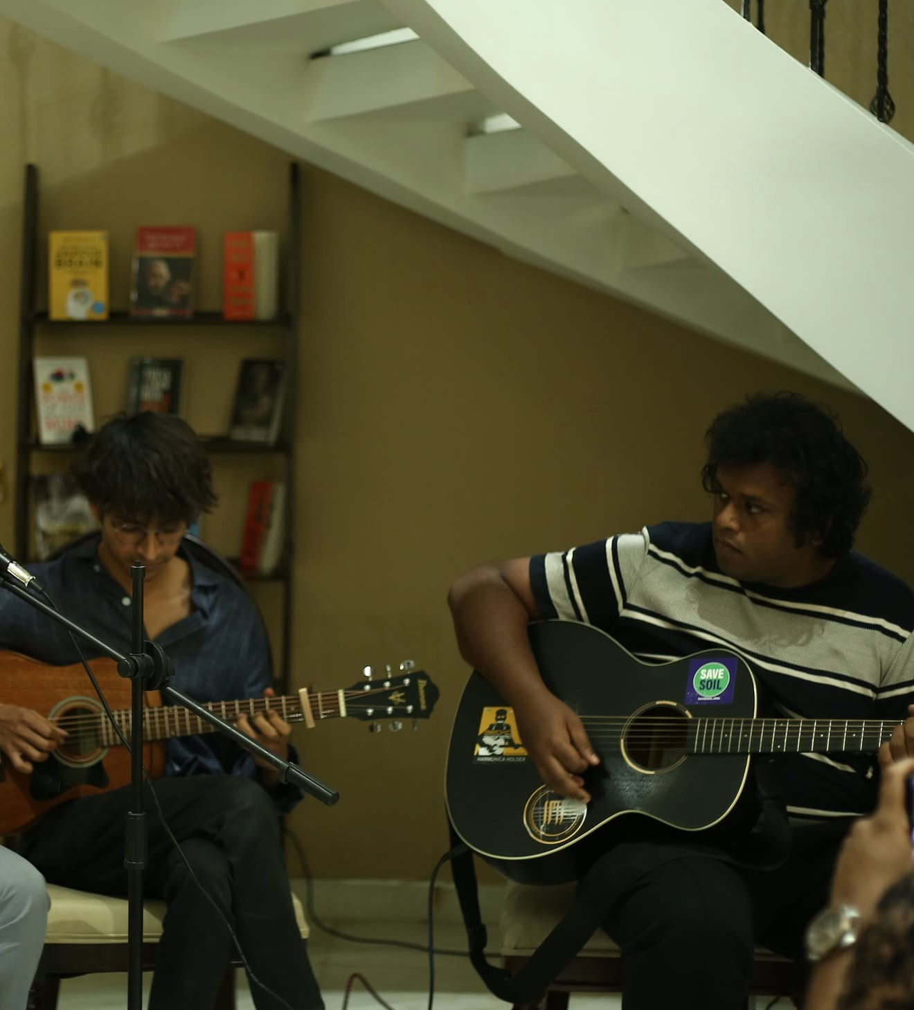 Two guitarists playing side by side next to a bookshelf